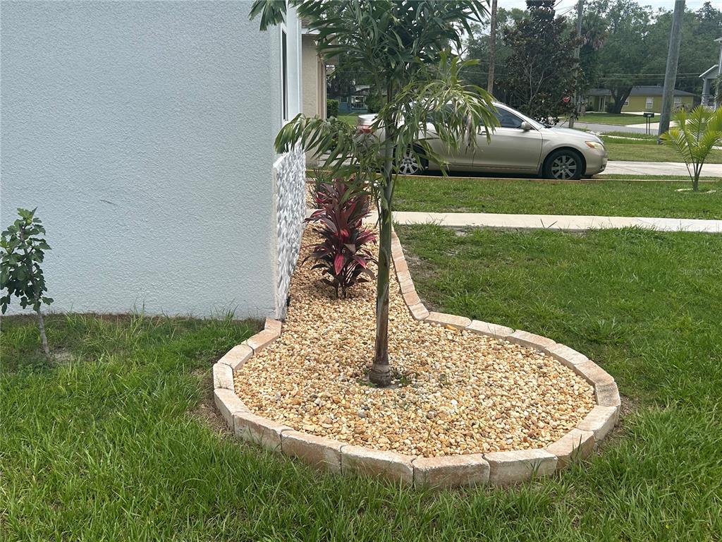 A landscaped garden bed with gravel, a small palm tree, and stone edging borders a house — 820 PECAN AVENUE, SANFORD, FL