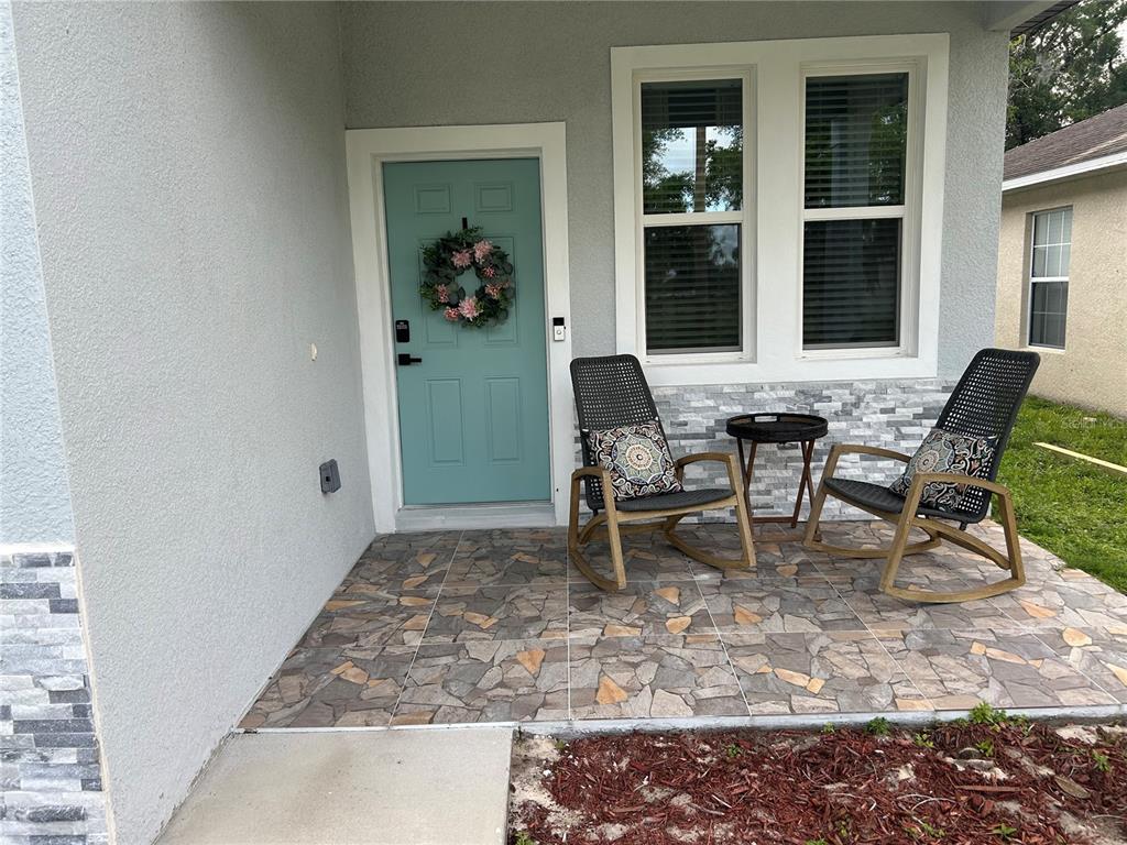 A front porch features a teal door, two rocking chairs, and stone-look tile flooring — 820 PECAN AVENUE, SANFORD, FL
