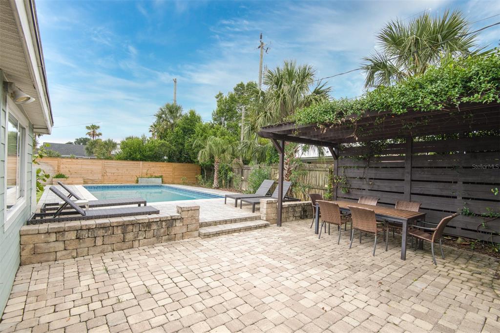 A backyard patio features a swimming pool, a wooden pergola, and a stone retaining wall — 159 SOUTHWIND CIRCLE, ST AUGUSTINE, FL