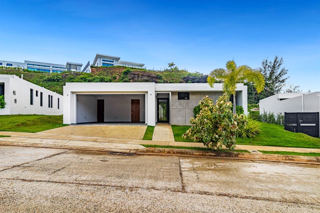 A modern, single-story house with a concrete facade, open garage, and a palm tree — 238 URB. MONTEAZUL, GUAYNABO, PR
