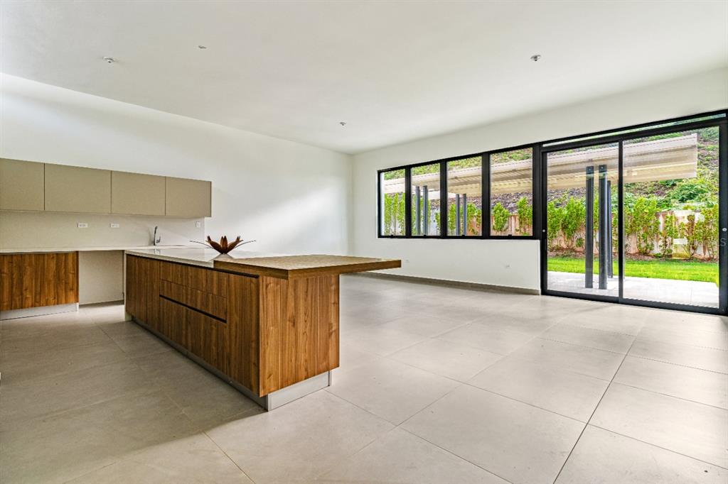 A modern kitchen features wood cabinetry, a large island, and floor-to-ceiling windows overlooking a yard — 238 URB. MONTEAZUL, GUAYNABO, PR