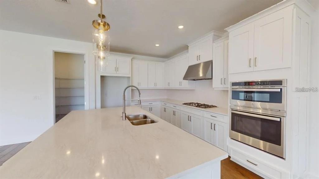 A modern kitchen features white cabinets, a large quartz island, and stainless steel appliances — 4911 CASERTA COURT, PALMETTO, FL