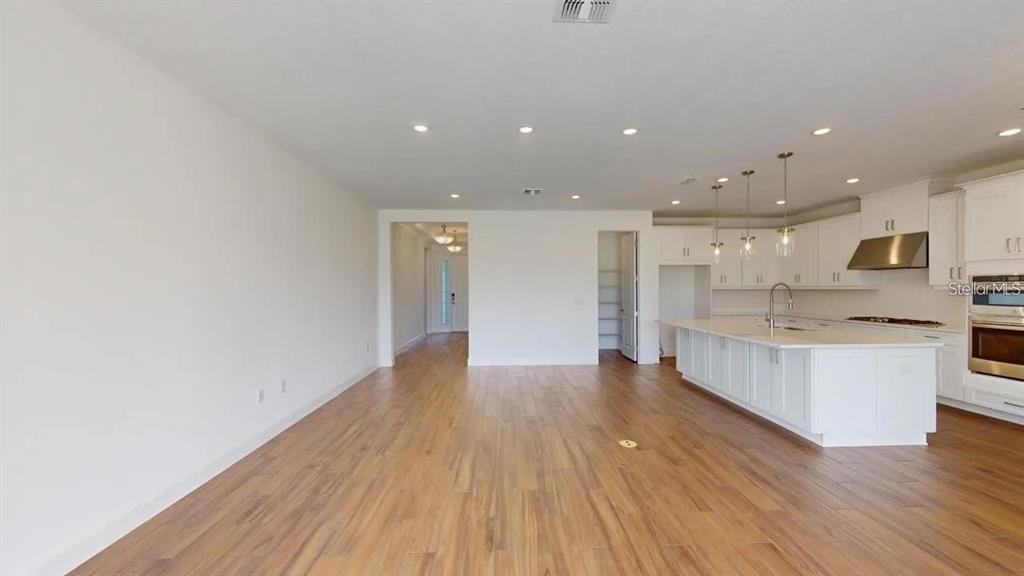 An open-concept kitchen and living area features white cabinetry, a large island, and wood flooring — 4911 CASERTA COURT, PALMETTO, FL