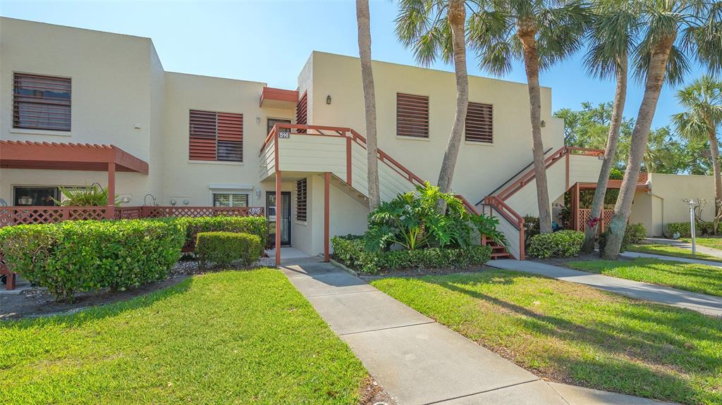 A two-story stucco apartment building features exterior staircases, wooden railings, and palm trees — 515 SPRING LAKES BOULEVARD UNIT 515, BRADENTON, FL