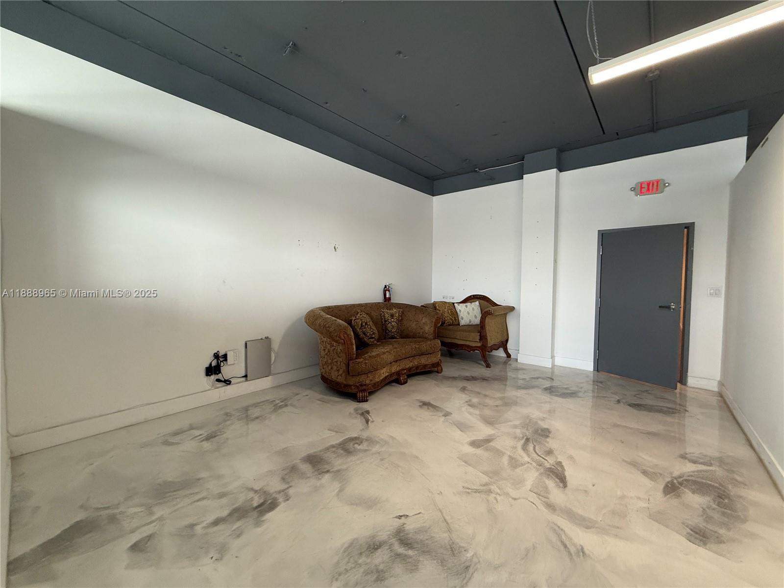An empty room features a grey epoxy floor, white walls, a dark ceiling, and two sofas — 42 NW 27th Ave # 302, Miami FL 33125, MIAMI, FL