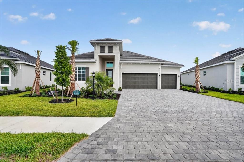 A single-story house with a gray tiled roof, a paved driveway, and a three-car garage — 19219 SCALLOP LOOP, LAKEWOOD RANCH, FL
