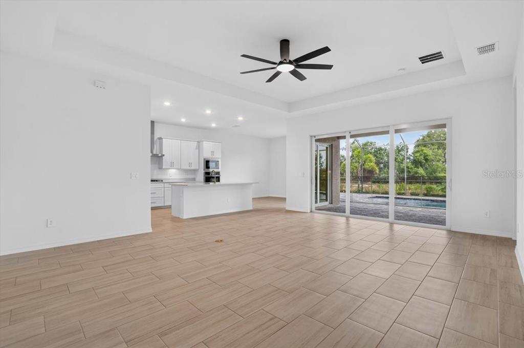 An open-concept living area features light wood-look tile flooring, a kitchen, and sliding glass doors — 19219 SCALLOP LOOP, LAKEWOOD RANCH, FL