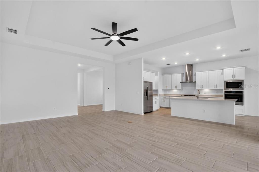 An open-concept kitchen and living area featuring white cabinetry, stainless steel appliances, and tile flooring — 19219 SCALLOP LOOP, LAKEWOOD RANCH, FL