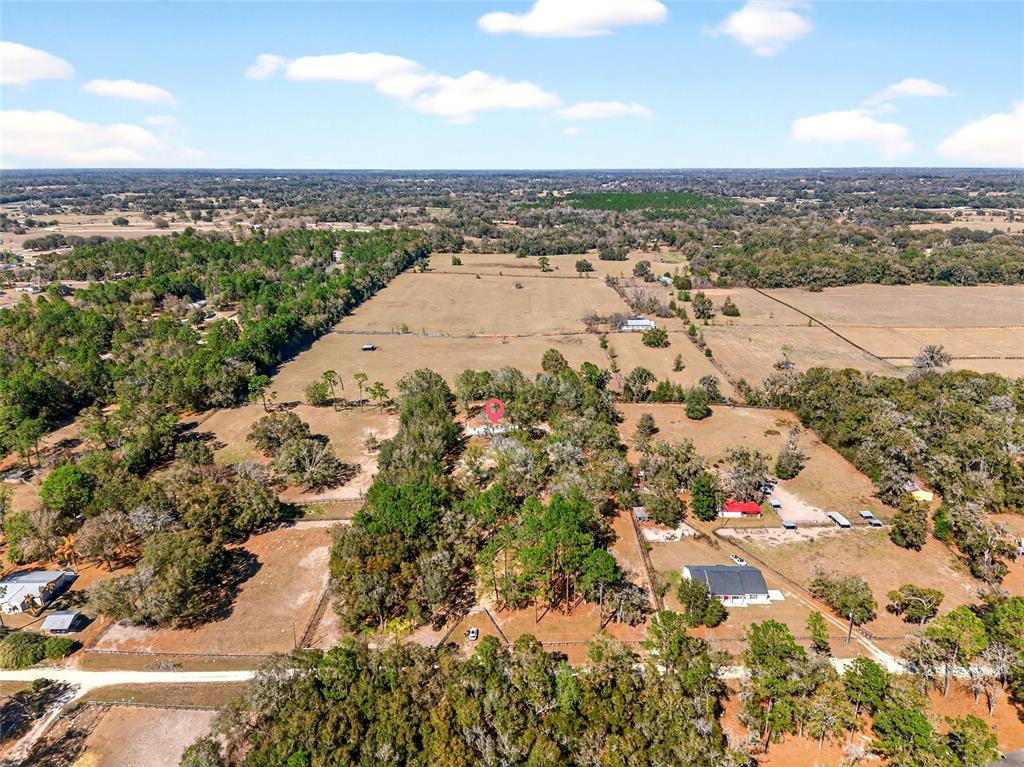 An aerial view shows a house with a red location pin amidst trees and fields — 10427 NW 8TH LANE, OCALA, FL