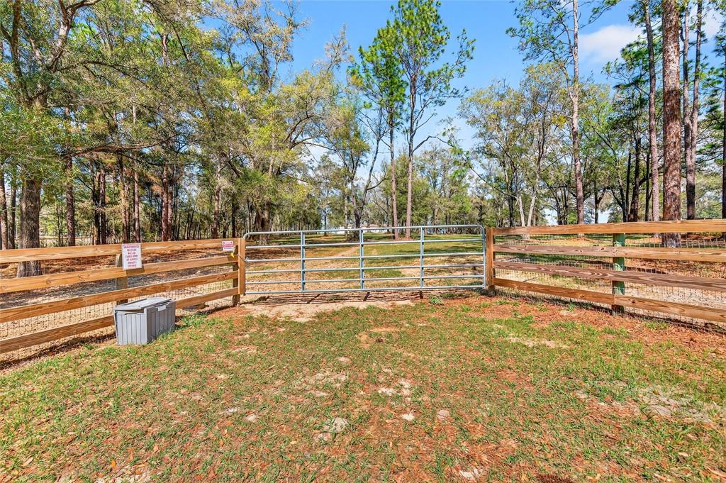 A metal gate connects wooden fences in a grassy, tree-lined outdoor area — 10427 NW 8TH LANE, OCALA, FL