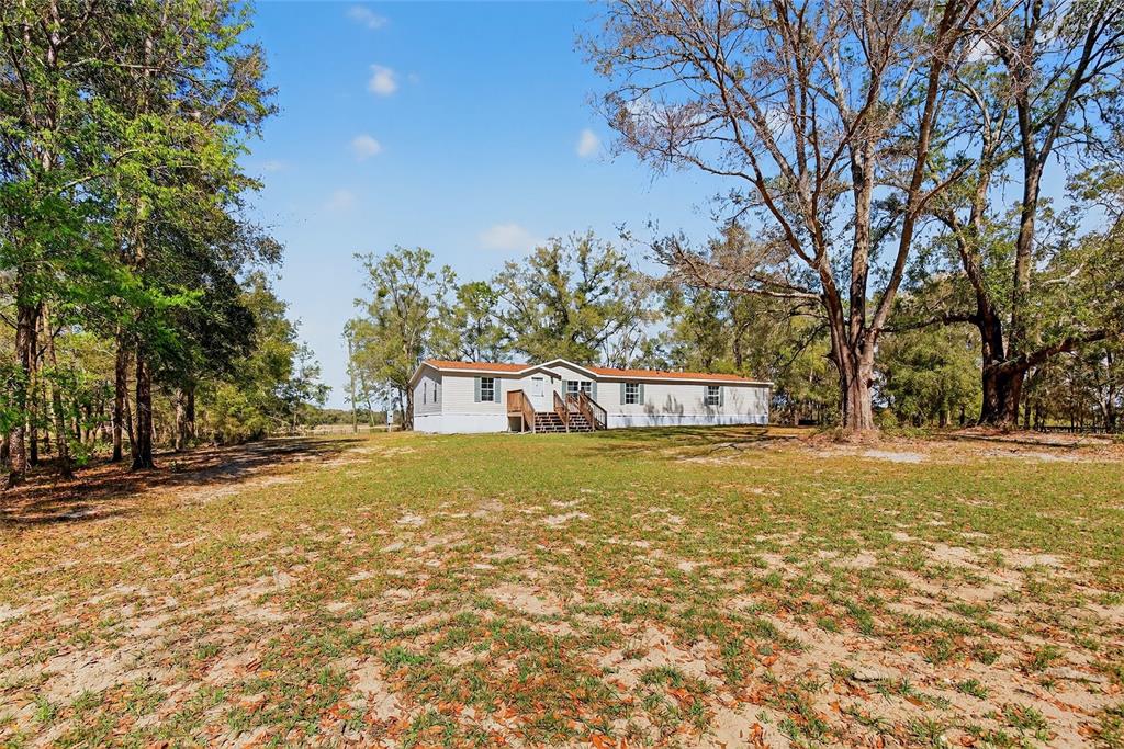 A single-story manufactured home sits on a large, grassy lot surrounded by mature trees — 10427 NW 8TH LANE, OCALA, FL