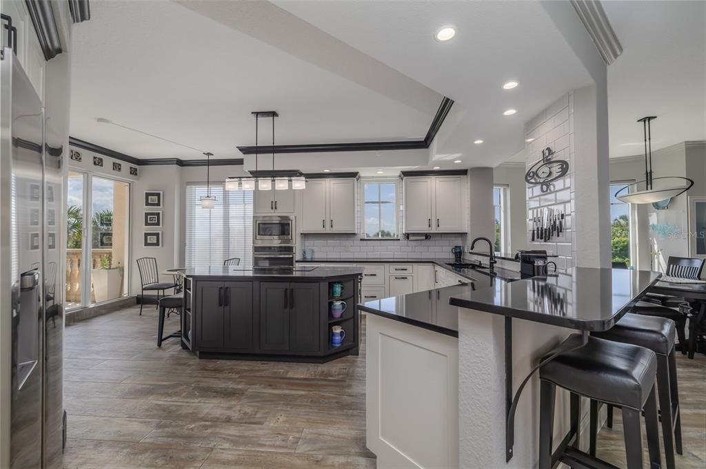 A modern kitchen features a dark island, white cabinetry, black countertops, and wood-look tile flooring — 261 MINORCA BEACH WAY UNIT 201, NEW SMYRNA BEACH, FL