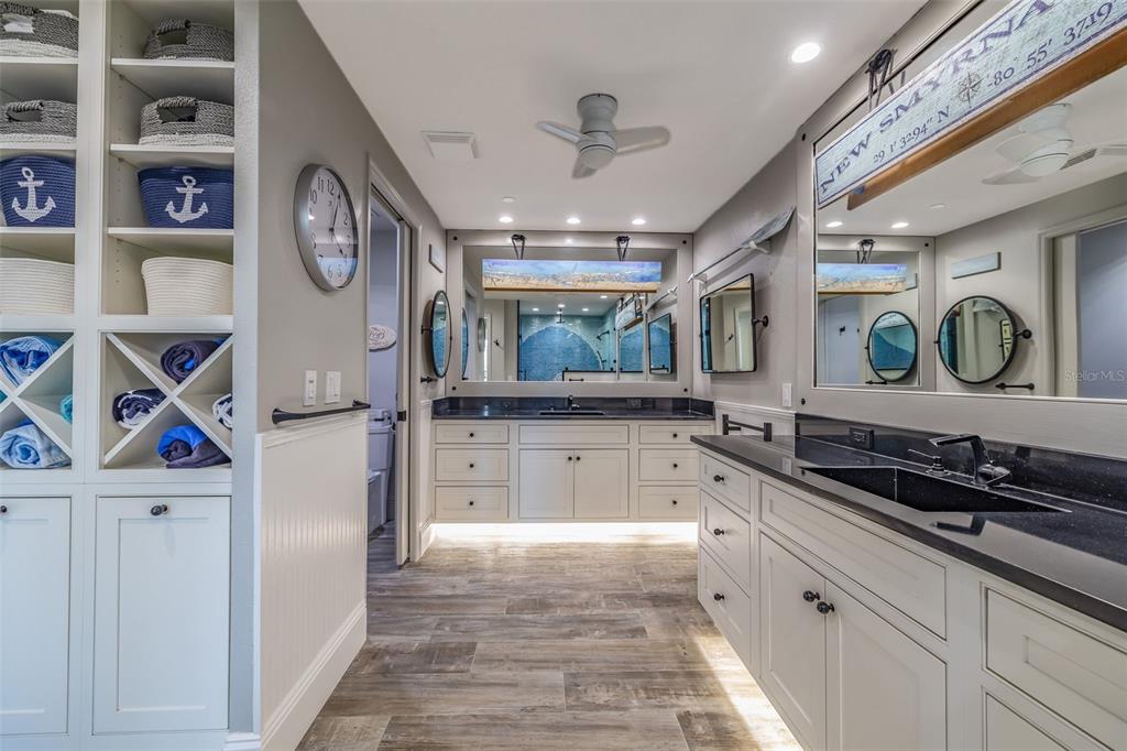 A coastal-themed bathroom features dual vanities with black countertops, white cabinetry, and built-in shelving — 261 MINORCA BEACH WAY UNIT 201, NEW SMYRNA BEACH, FL