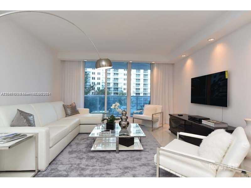A modern living room features a white sectional sofa, glass coffee table, and wall-mounted television — 2301 Collins Ave # 617, Miami Beach FL 33139, MIAMI BEACH, FL