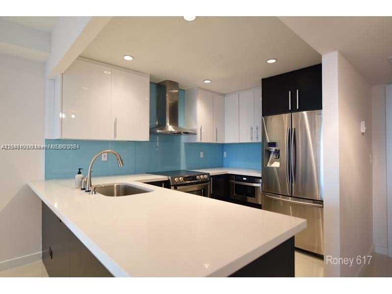 A modern kitchen features white cabinets, stainless steel appliances, and a light blue glass backsplash — 2301 Collins Ave # 617, Miami Beach FL 33139, MIAMI BEACH, FL