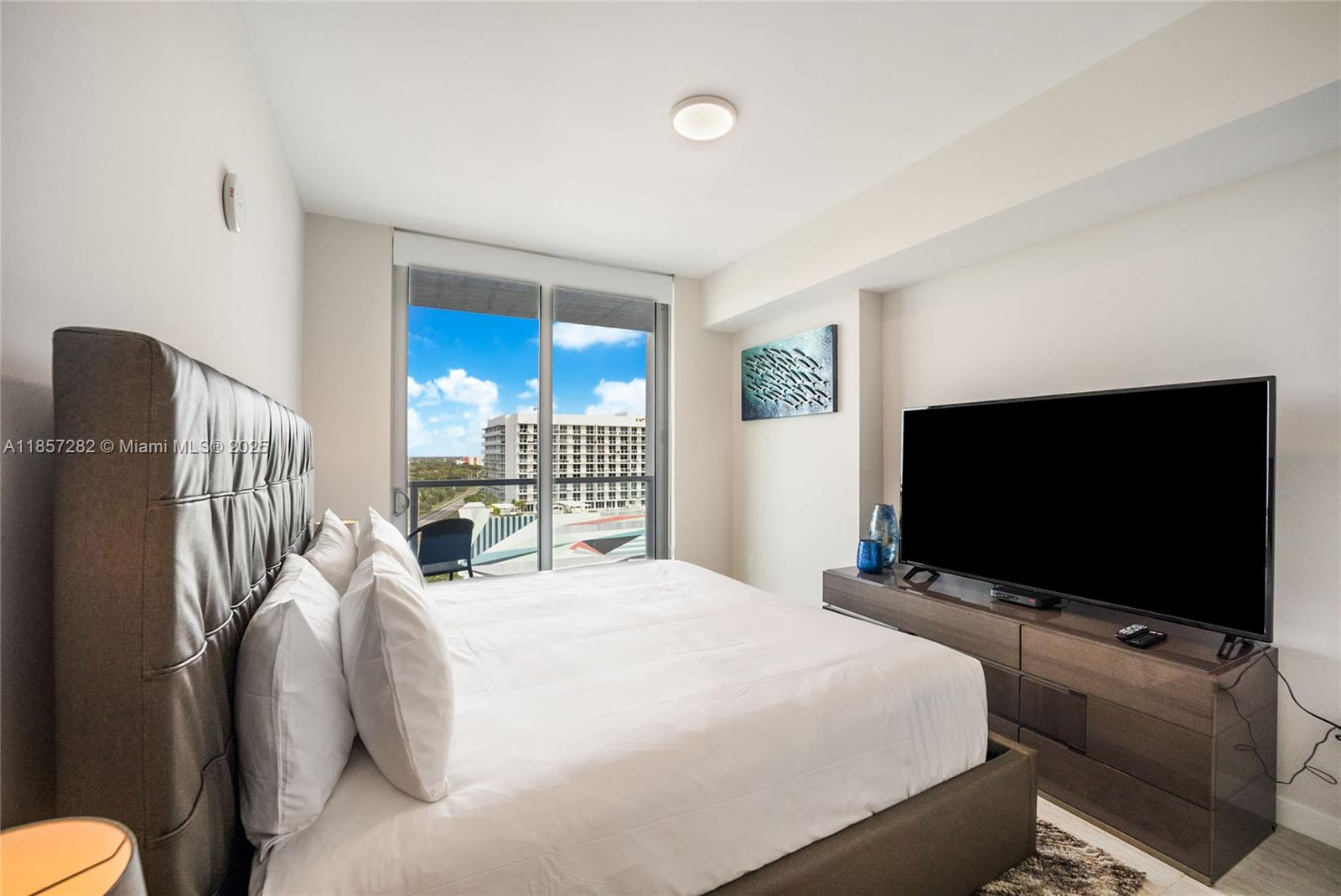 A bedroom features a bed, a television on a dresser, and a balcony with city views — 3900 Biscayne Blvd # 1009, Miami FL 33137, MIAMI, FL