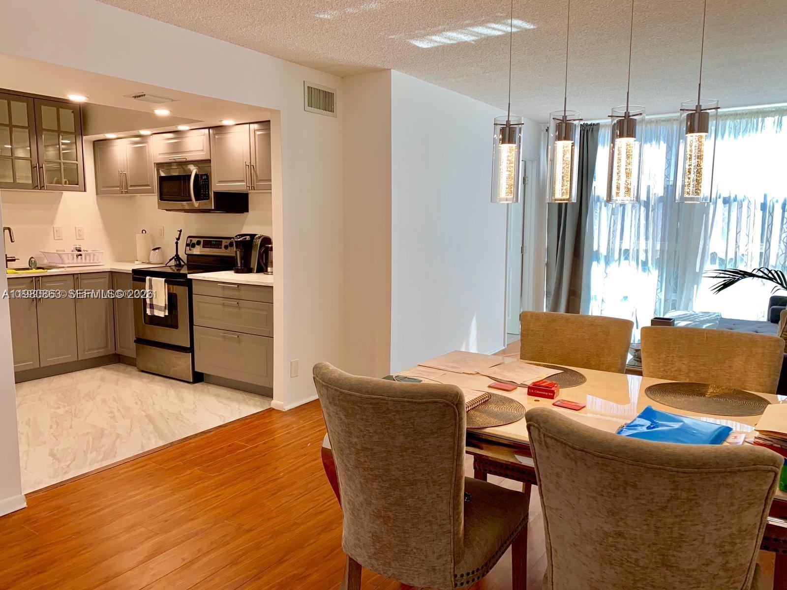 A kitchen with gray cabinets and stainless steel appliances opens into a dining area — 851 Three Islands Blvd # 308, Hallandale Beach FL 33009, HALLANDALE BEACH, FL