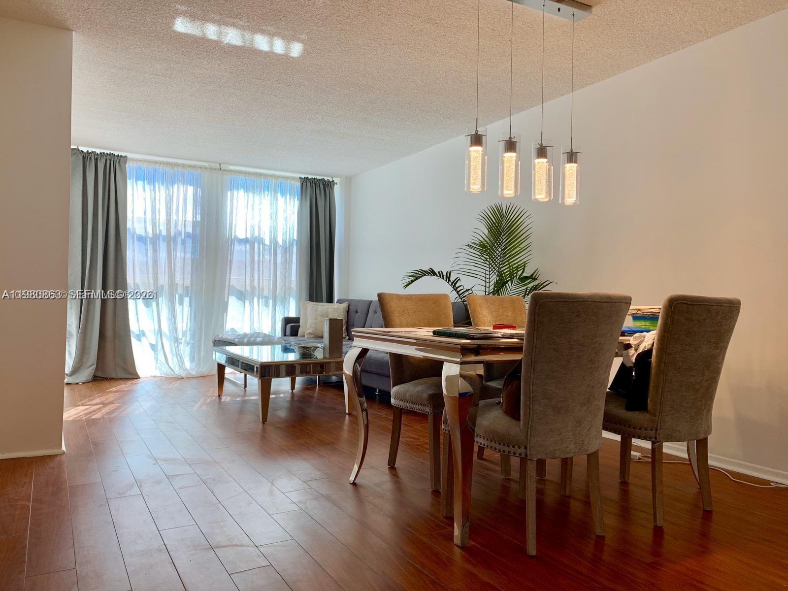 A dining area with a modern table and chairs sits next to a living room — 851 Three Islands Blvd # 308, Hallandale Beach FL 33009, HALLANDALE BEACH, FL