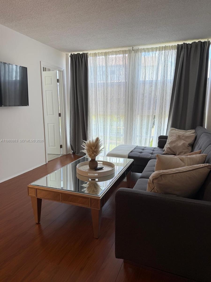 A living room features a dark gray sectional sofa, a mirrored coffee table, and floor-to-ceiling curtains — 851 Three Islands Blvd # 308, Hallandale Beach FL 33009, HALLANDALE BEACH, FL