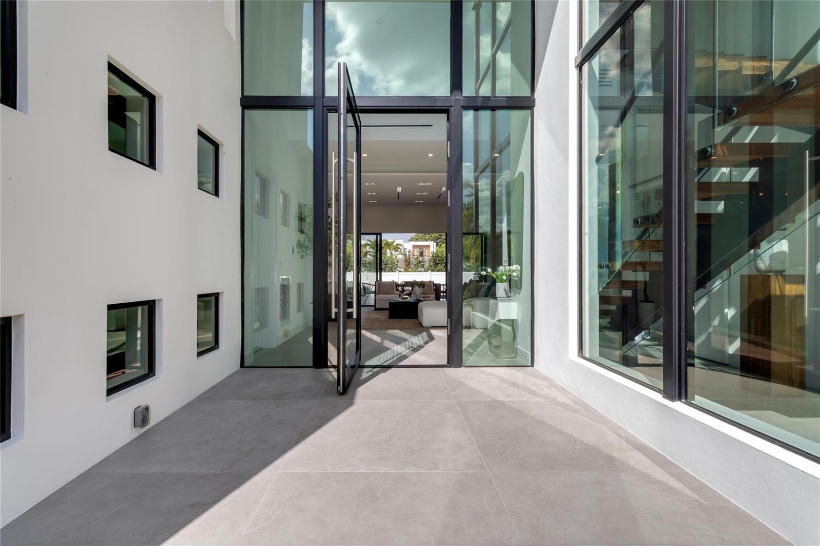 A modern entryway with large glass panels, a pivoting door, and gray tile flooring — 3205 Leigh Road, Pompano Beach FL 33062, POMPANO BEACH, FL