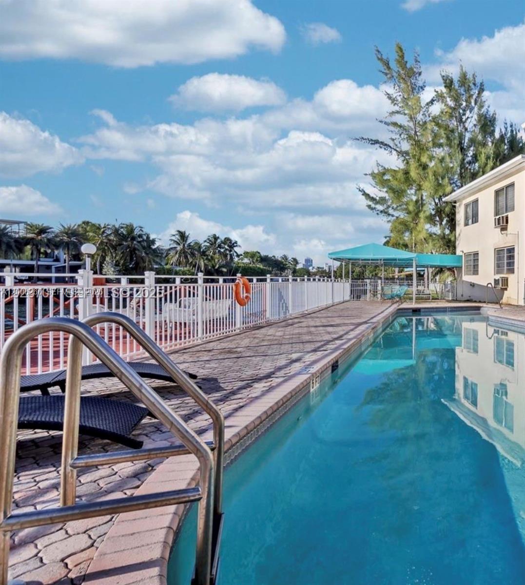 A narrow outdoor swimming pool runs alongside a multi-story building with a white fence — 4740 Pine Tree Dr # 20, Miami Beach FL 33140, MIAMI BEACH, FL