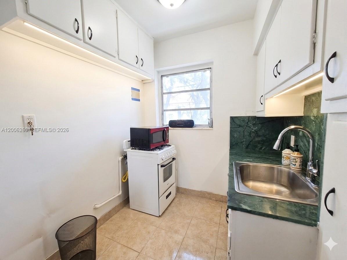 A small kitchen features white cabinets, a green marble countertop, and a white gas stove — 4740 Pine Tree Dr # 20, Miami Beach FL 33140, MIAMI BEACH, FL
