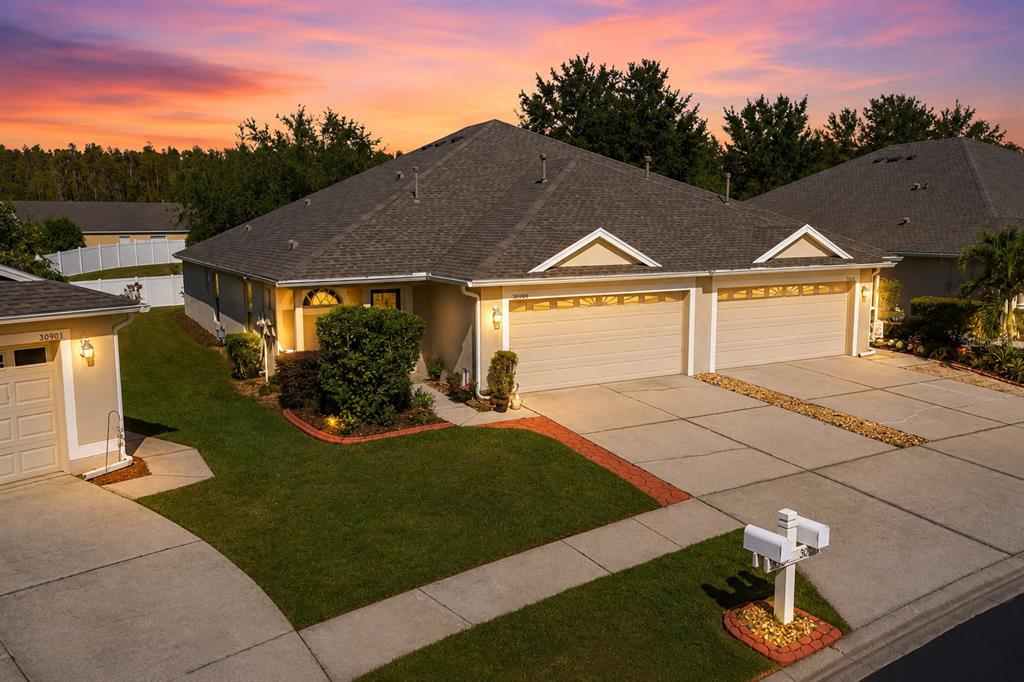 An aerial view of a duplex home with two garage doors and a sunset sky — 30907 WHITLOCK DRIVE, WESLEY CHAPEL, FL