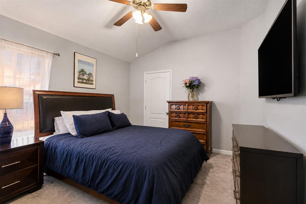 A bedroom features a dark wood bed frame, a wooden dresser, and a wall-mounted television — 30907 WHITLOCK DRIVE, WESLEY CHAPEL, FL