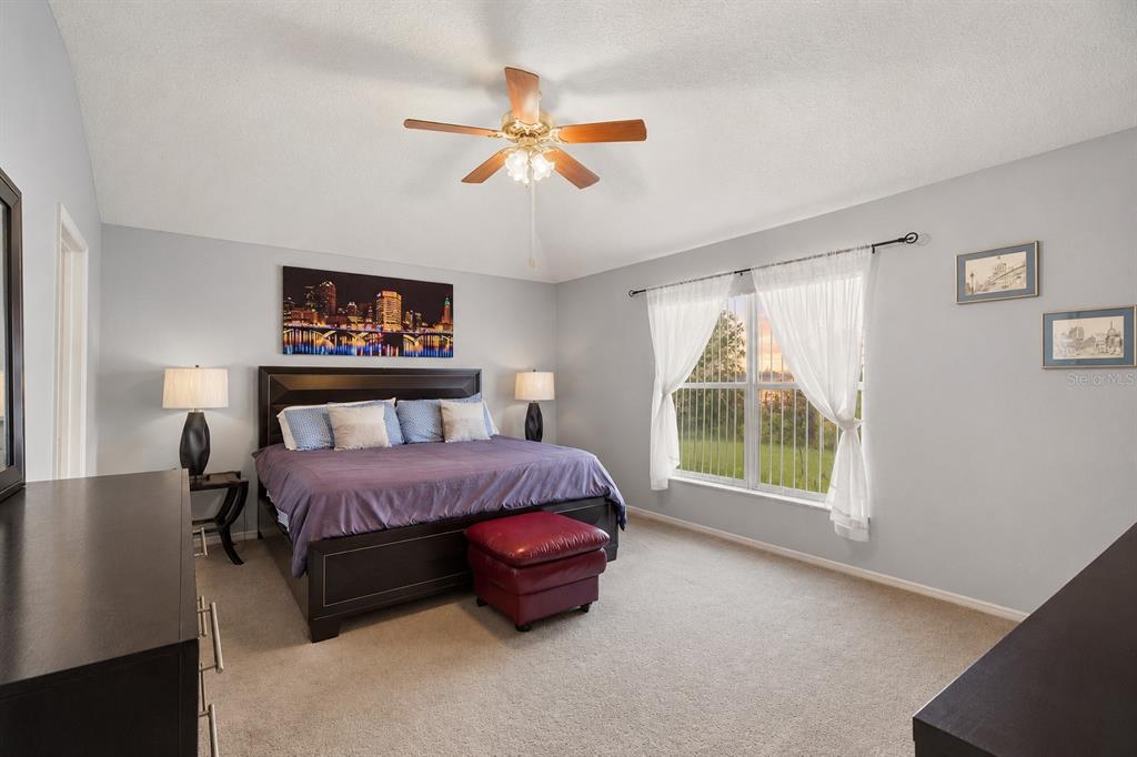 A bedroom features a king-sized bed, a red ottoman, a ceiling fan, and a large window — 30907 WHITLOCK DRIVE, WESLEY CHAPEL, FL
