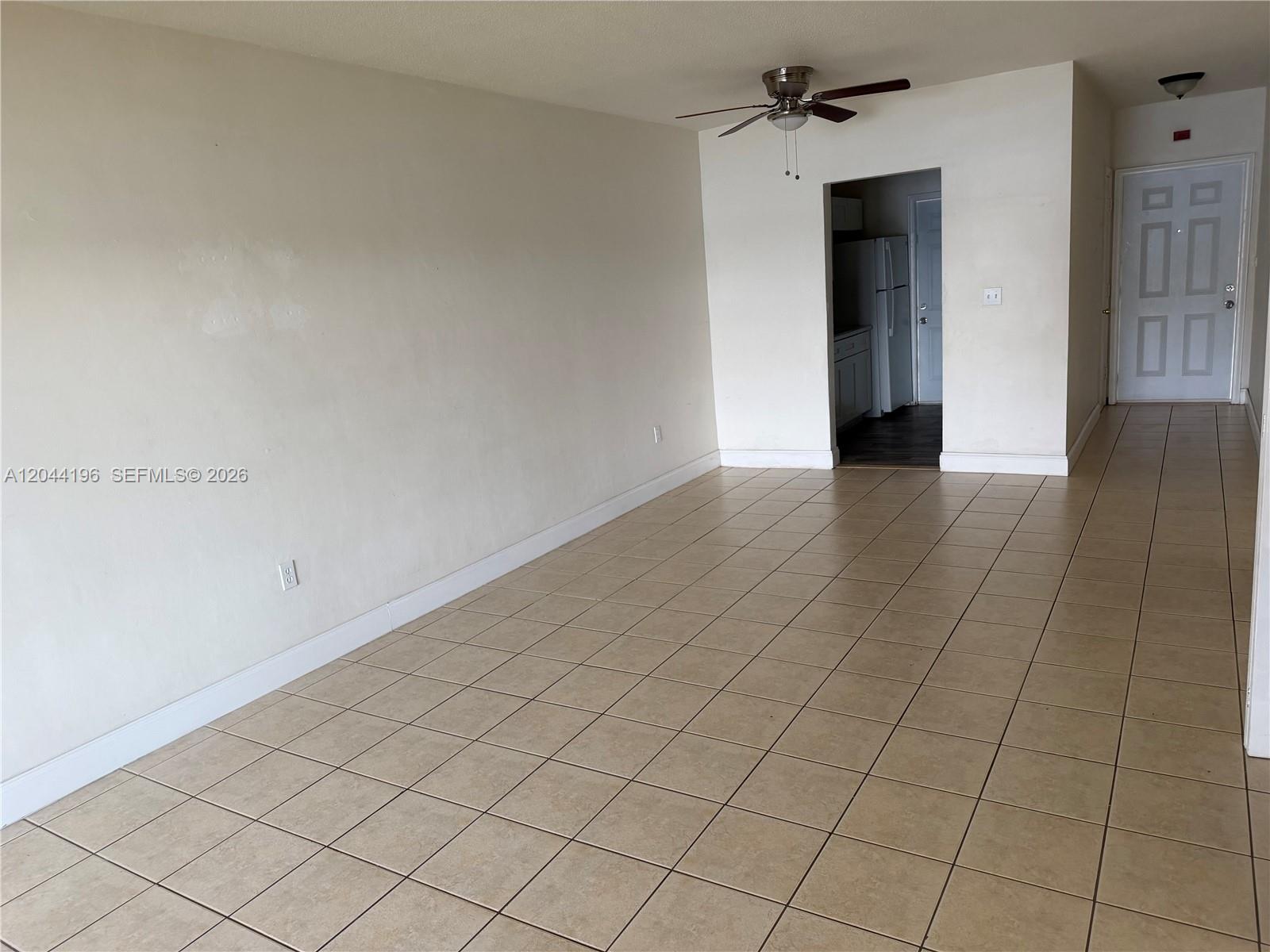 An empty room features beige tile flooring, white walls, a ceiling fan, and a kitchen doorway — 19001 NE 2nd Ave # 1404, Miami FL 33179, MIAMI, FL