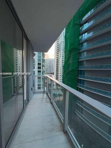 A balcony with a glass railing overlooks a neighboring high-rise building covered in green netting — 77 SE 5th St # 2004, Miami FL 33131, MIAMI, FL