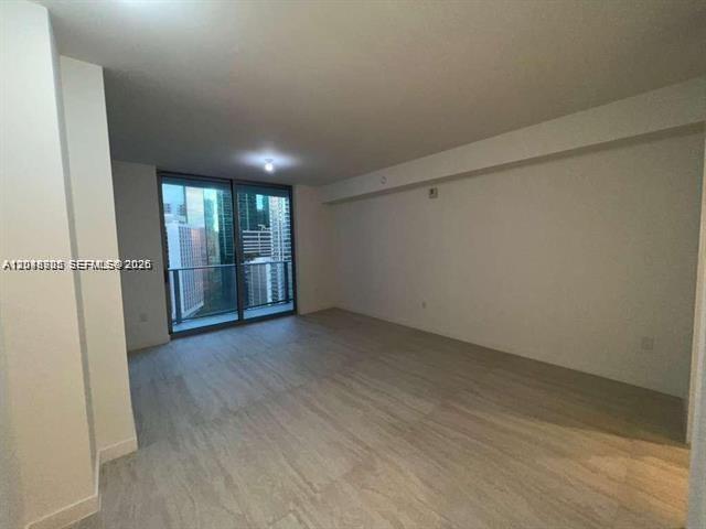 An empty room with light-colored wood-look flooring and a large glass sliding door — 77 SE 5th St # 2004, Miami FL 33131, MIAMI, FL