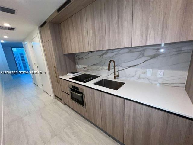 A modern kitchen features wood-grain cabinetry, white countertops, and a marble-patterned backsplash — 77 SE 5th St # 2004, Miami FL 33131, MIAMI, FL