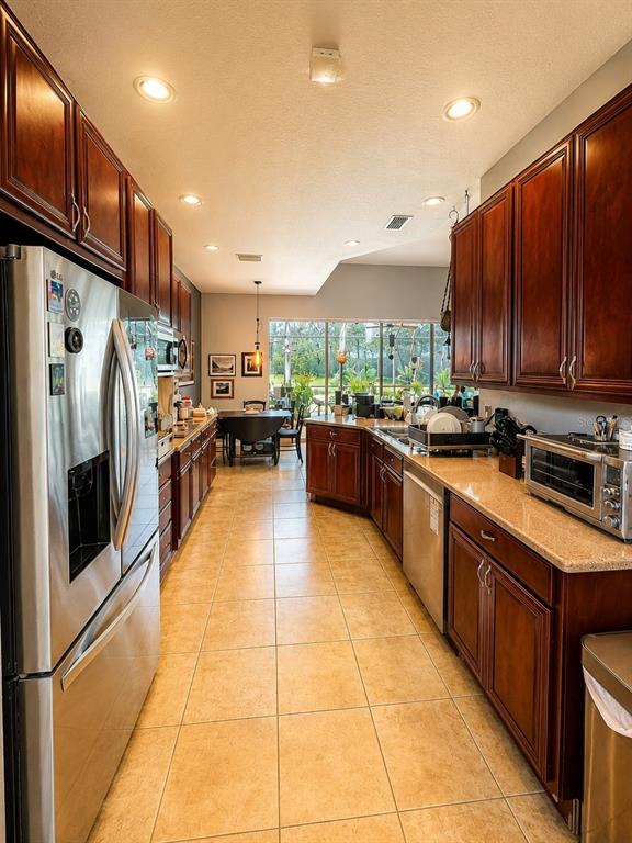 A galley kitchen features dark wood cabinets, granite countertops, stainless steel appliances, and tile flooring — 10703 BANFIELD DRIVE, RIVERVIEW, FL