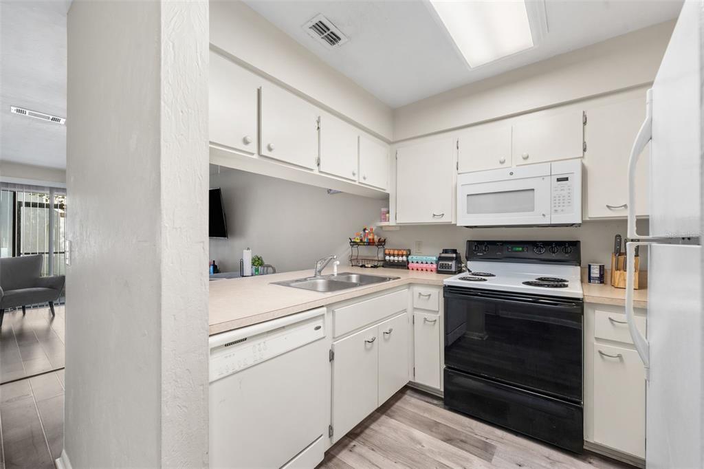 A kitchen features white cabinets, a black stove, a white dishwasher, and light-colored countertops — 2635 SW 35TH PLACE UNIT 307, GAINESVILLE, FL