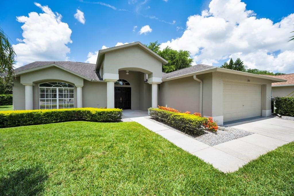 A single-story house with a beige stucco exterior, a two-car garage, and a landscaped front yard — 1253 EVENINGSIDE COURT, TRINITY, FL