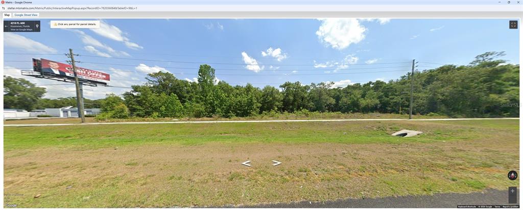 This is a Google Street View image of a vacant, grassy lot with trees behind it — S ORANGE BLOSSOM TRAIL, KISSIMMEE, FL
