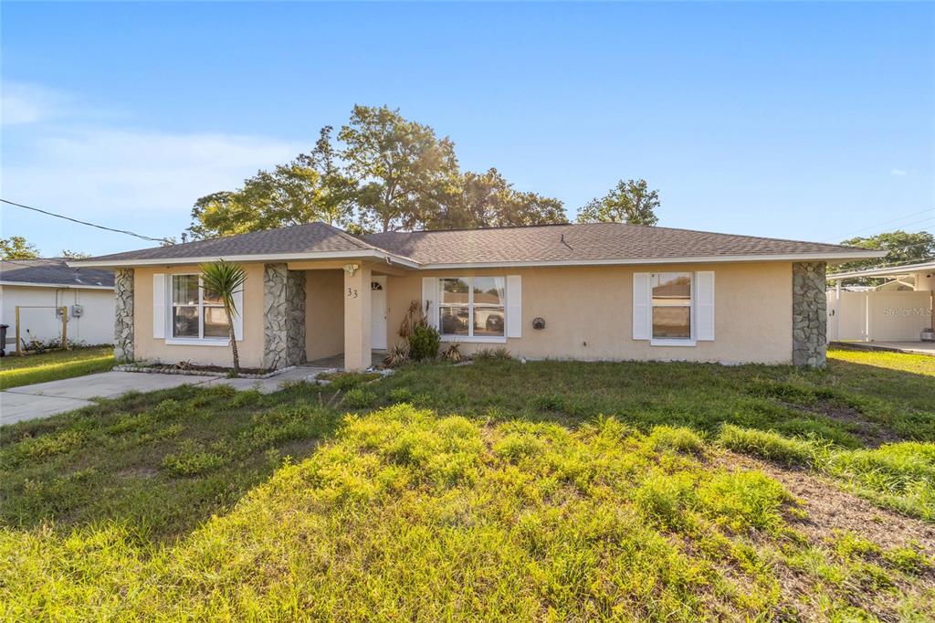 A single-story house with a beige stucco exterior, stone accents, and a shingled roof — 33 PECAN RUN PASS, OCALA, FL
