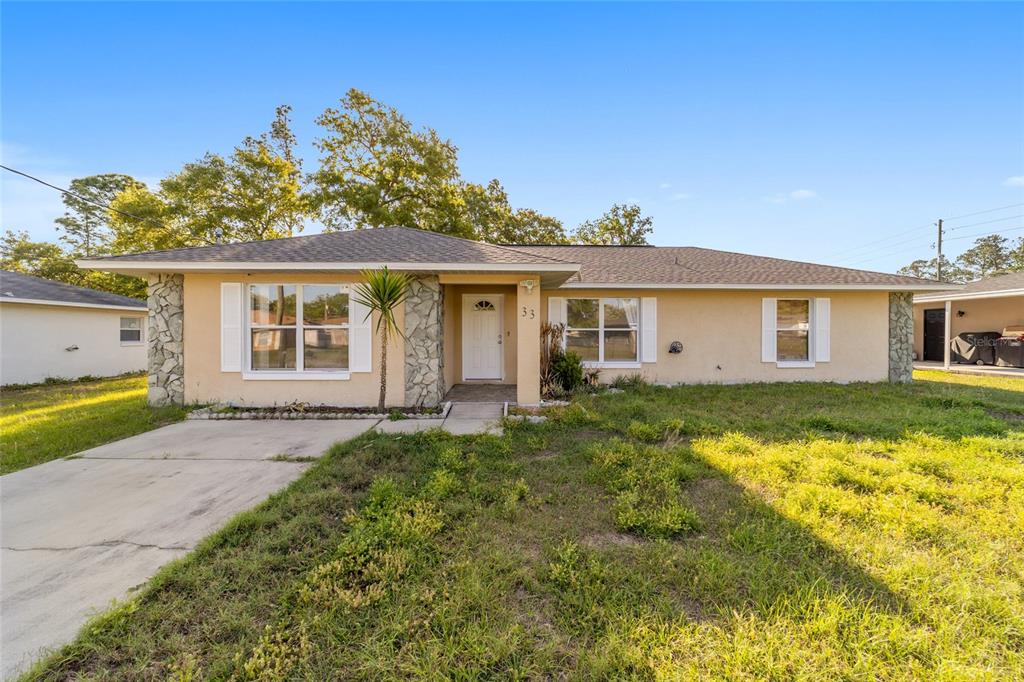 A single-story house with a beige stucco exterior, stone accents, and a concrete driveway — 33 PECAN RUN PASS, OCALA, FL