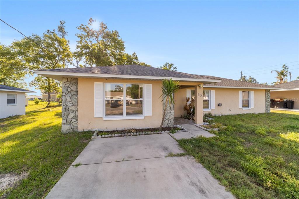 A single-story house with tan stucco, stone accents, and a concrete driveway under a clear sky — 33 PECAN RUN PASS, OCALA, FL