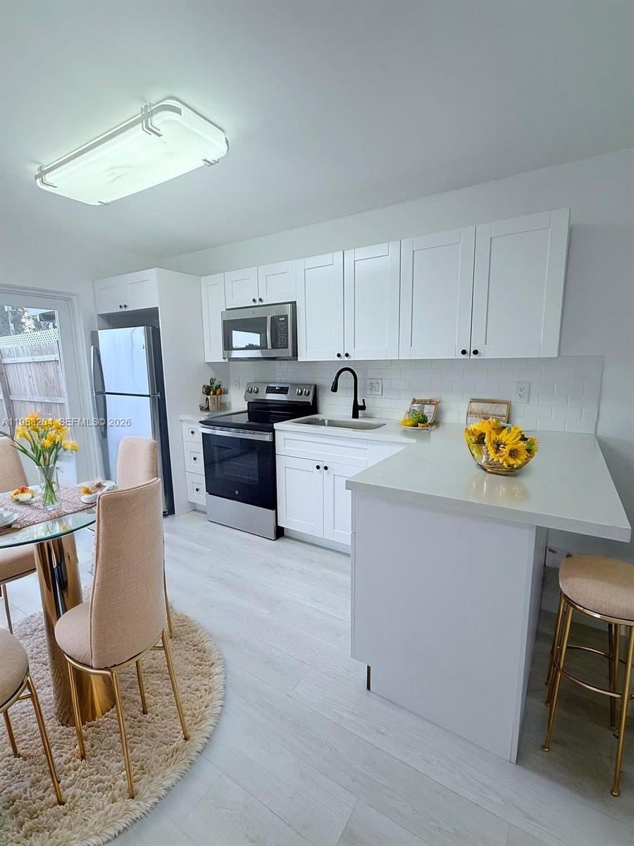 A modern kitchen features white cabinetry, stainless steel appliances, and a white peninsula countertop — 6801 W 36th Ave # 102, Hialeah FL 33018, HIALEAH, FL