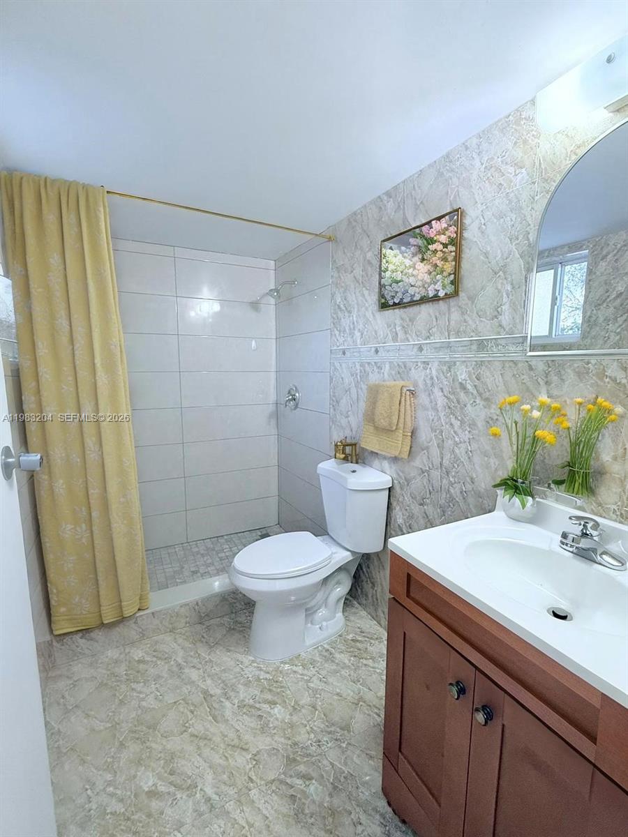 A bathroom features a walk-in shower with a yellow curtain, a toilet, and a vanity — 6801 W 36th Ave # 102, Hialeah FL 33018, HIALEAH, FL
