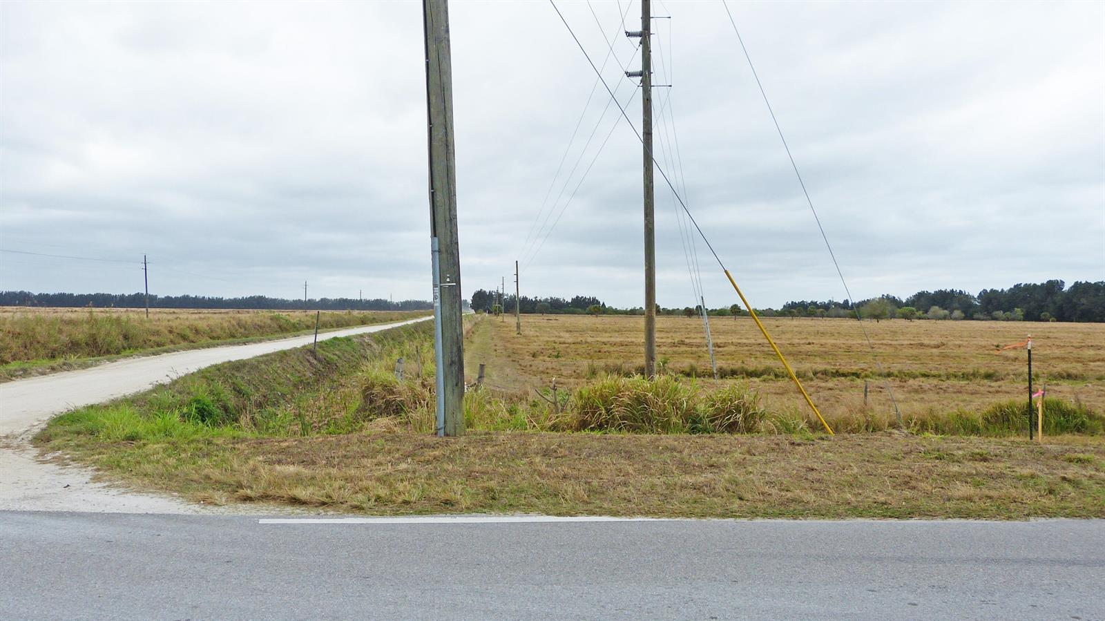 A gravel road runs alongside a grassy field with utility poles under a cloudy sky — Tbd S Header Canal Road, Fort Pierce FL 34945, FORT PIERCE, FL