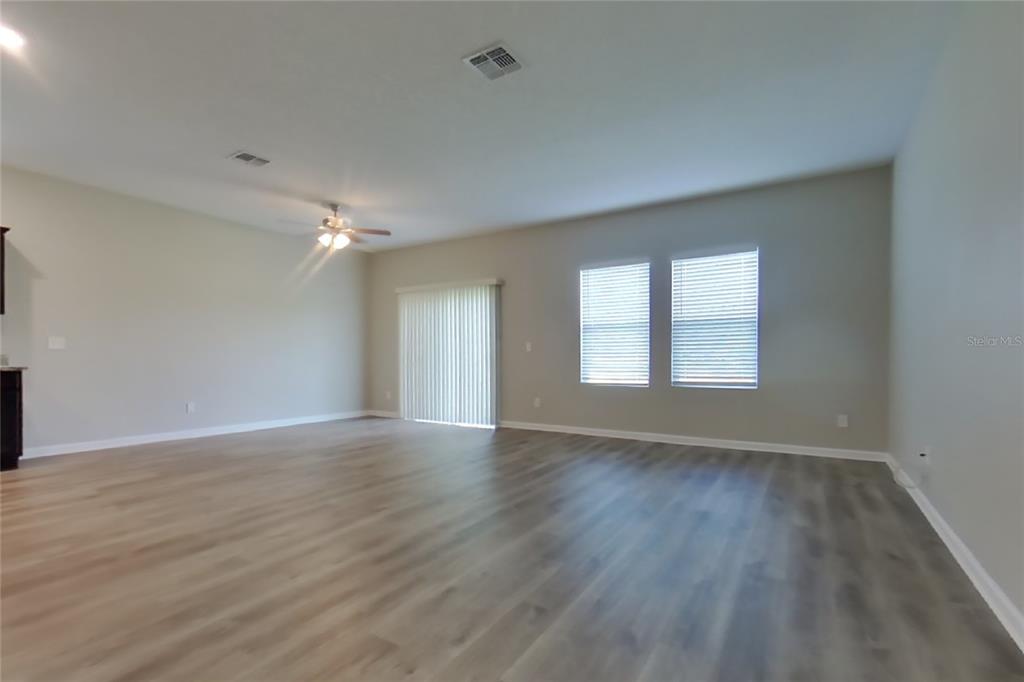 An empty living room features light wood-look flooring, neutral walls, a ceiling fan, and sliding doors — 16517 CHERRY LANDING DRIVE, GROVELAND, FL