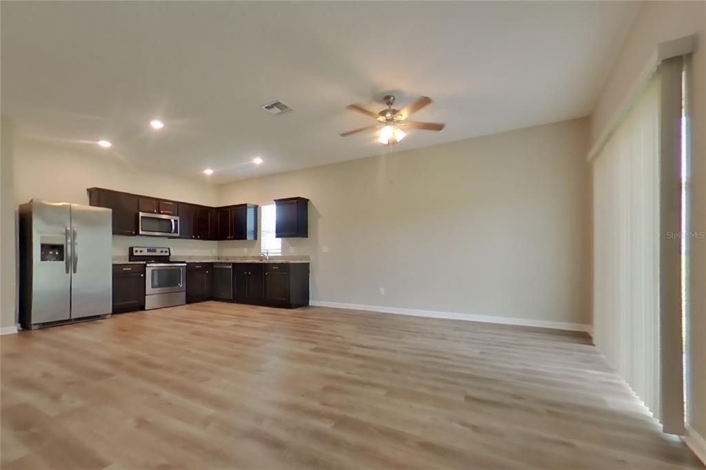 An open-concept kitchen and living area features dark wood cabinets, stainless steel appliances, and flooring — 16517 CHERRY LANDING DRIVE, GROVELAND, FL