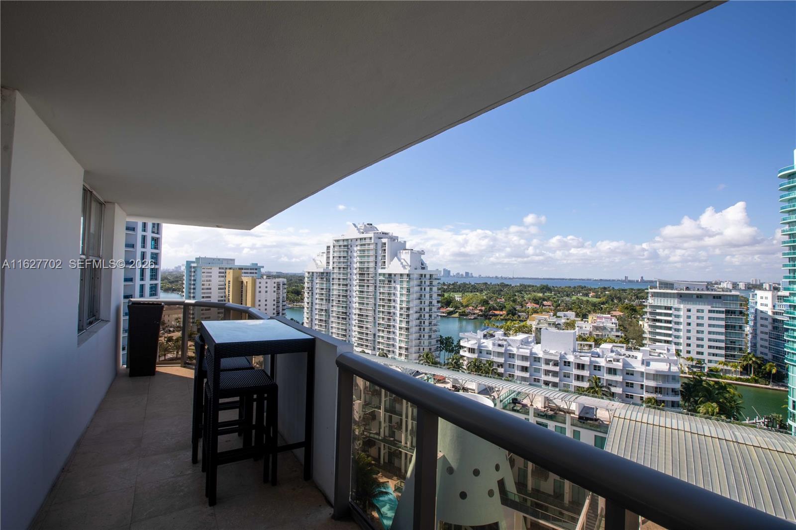 A balcony with a small table and chairs overlooks a city skyline and water — 6039 Collins Ave # 1728, Miami Beach FL 33140, MIAMI BEACH, FL
