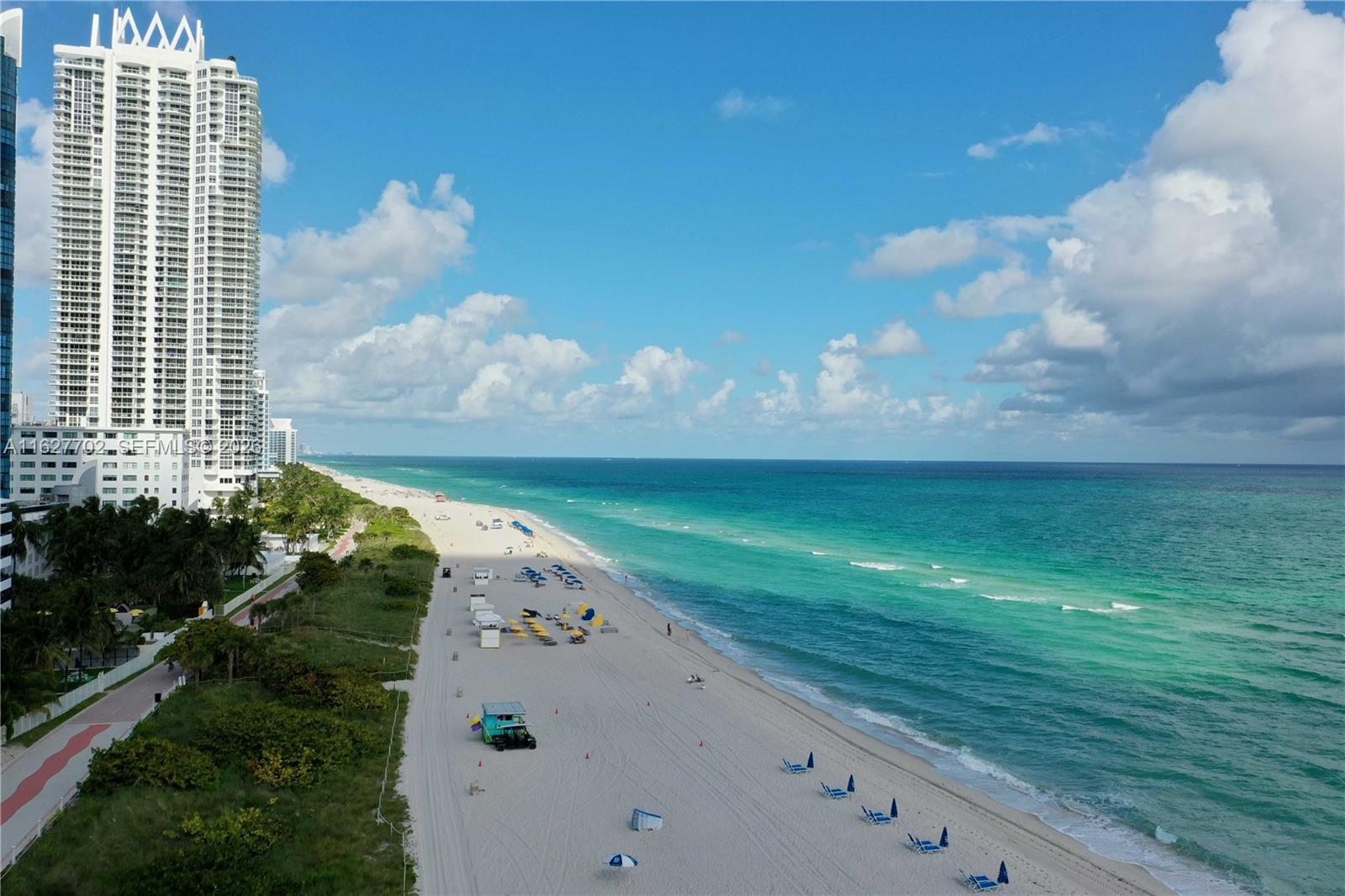 An aerial view shows a sandy beach with lounge chairs next to a tall skyscraper — 6039 Collins Ave # 1728, Miami Beach FL 33140, MIAMI BEACH, FL