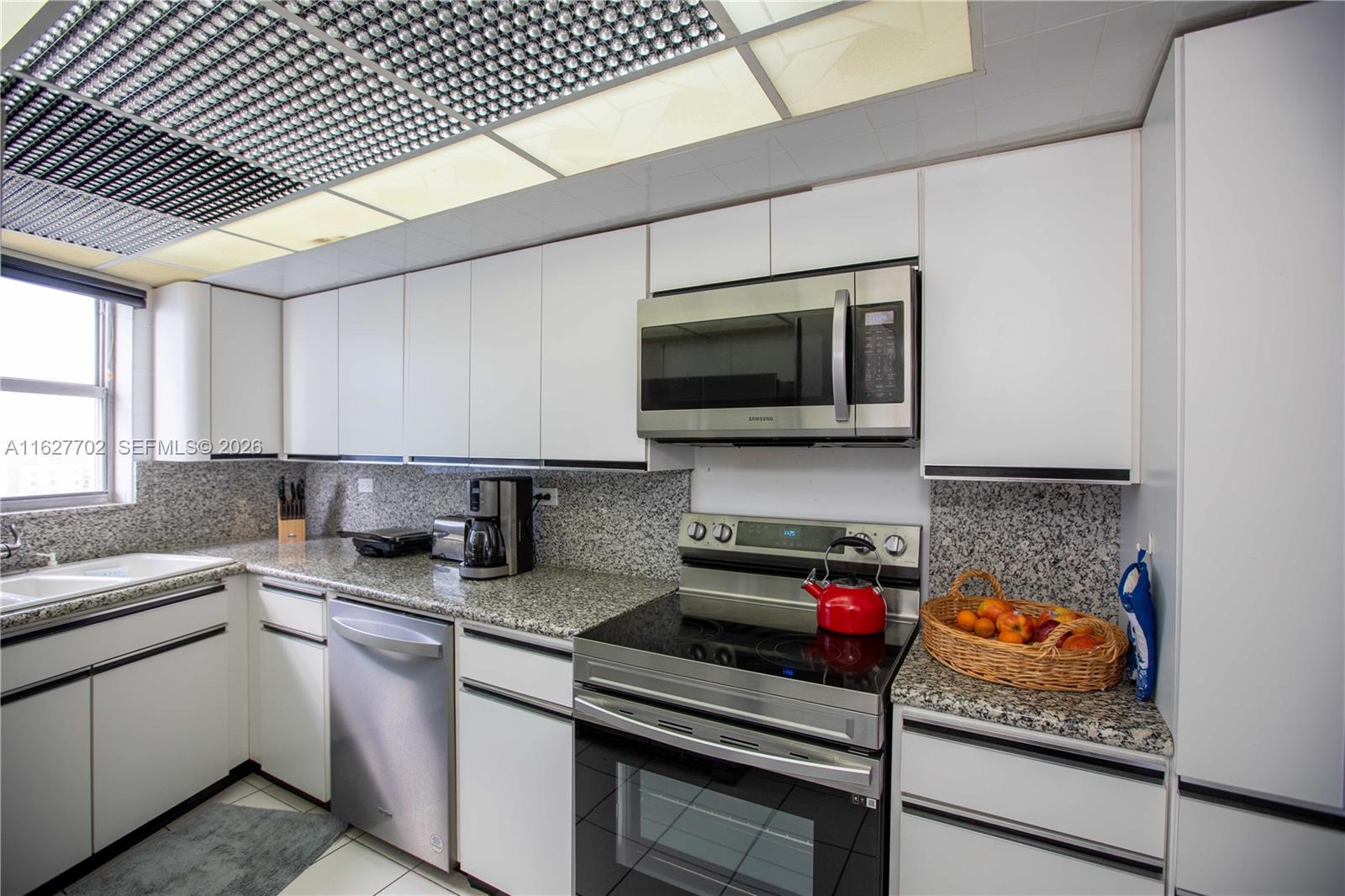 A kitchen features white cabinetry, granite countertops, stainless steel appliances, and a grid ceiling light — 6039 Collins Ave # 1728, Miami Beach FL 33140, MIAMI BEACH, FL