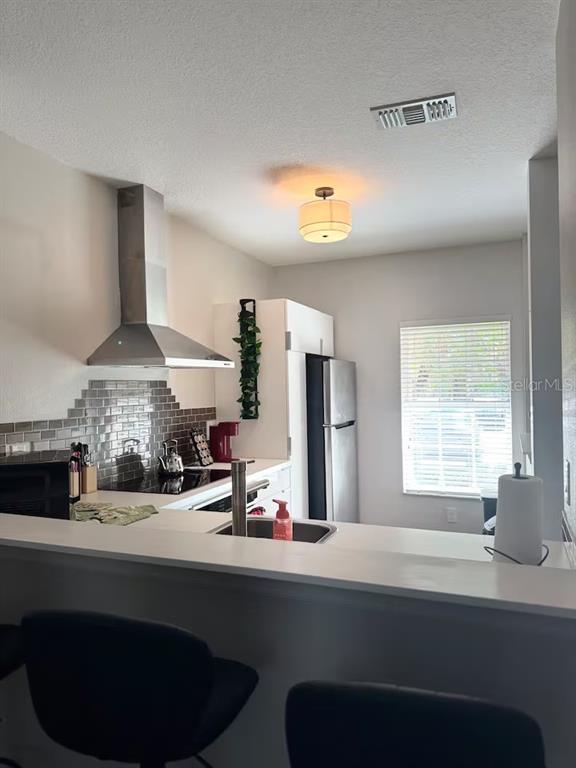 A kitchen features a stainless steel range hood, gray tile backsplash, and a breakfast bar — 774 CHELSEA DRIVE, DAVENPORT, FL