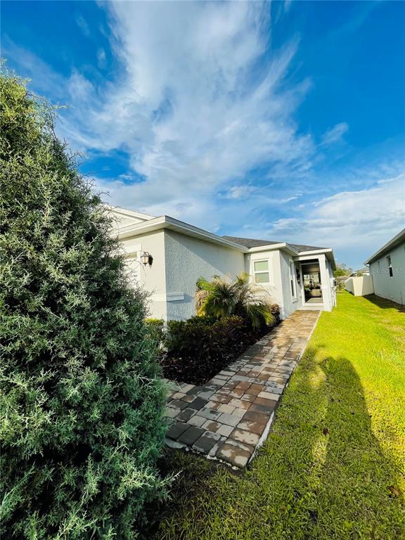 A paved walkway leads to the side entrance of a light-colored house with landscaping — 2818 SANCTUARY DRIVE, CLERMONT, FL